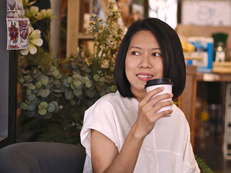 Portraits of Asian woman holding a cup of coffee looking to her right hand with smile face in cozy...