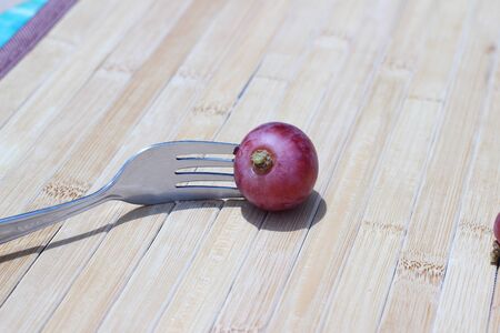 The grapes are plugged with a fork resting on brown backgroundの写真素材