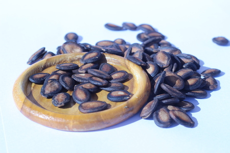 Watermelon seeds piled in brown wooden plate on a white backgroundの写真素材