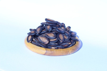 Watermelon seeds piled in brown wooden plate on a white backgroundの写真素材