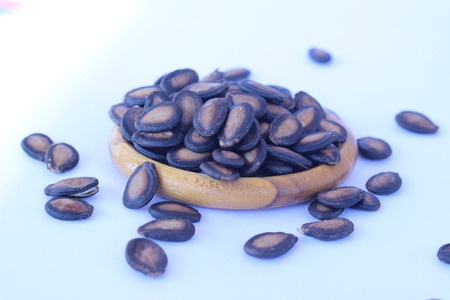 Watermelon seeds piled in brown wooden plate on a white backgroundの写真素材