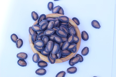 Watermelon seeds piled in brown wooden plate on a white backgroundの写真素材