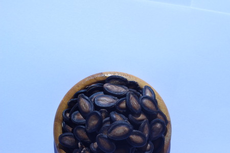 Watermelon seeds piled in brown wooden plate on a white backgroundの写真素材