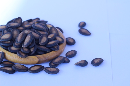 Watermelon seeds piled in brown wooden plate on a white backgroundの写真素材