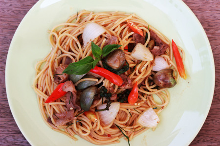 Stir spa-style spaghetti with Thai style meat in a green dish on a brown backgroundの写真素材