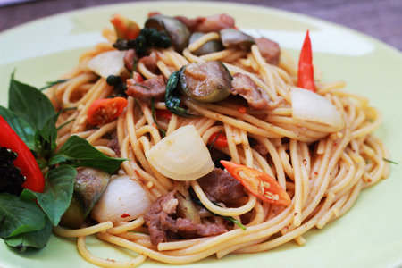 Stir spa-style spaghetti with Thai style meat in a green dish on a brown backgroundの写真素材