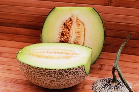 Melon fruit is spherical, has a rough texture and delicious sweet taste is cut on  brown background.