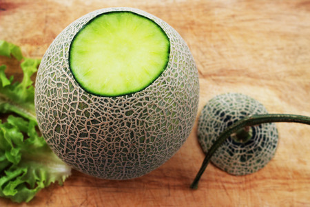 Melon fruit is spherical, has a rough texture and delicious sweet taste is cut on  brown background.の写真素材