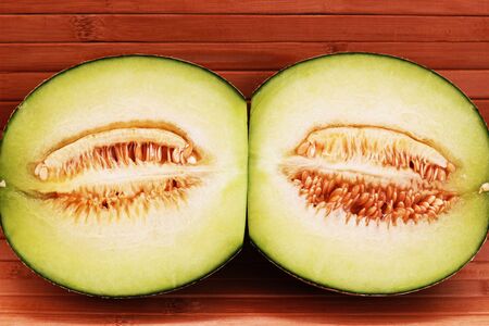 Melon fruit is spherical, has a rough texture and delicious sweet taste is cut on  brown background.