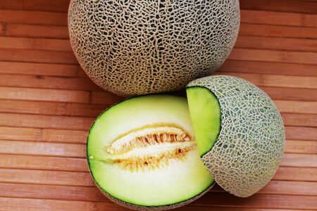 Melon fruit is spherical, has a rough texture and delicious sweet taste is cut on  brown background.の写真素材