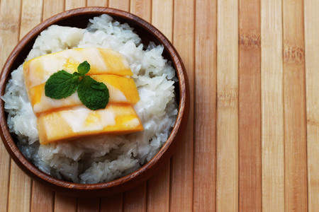 Mango sticky rice is put in a wooden container placed on a brown wooden tableの写真素材