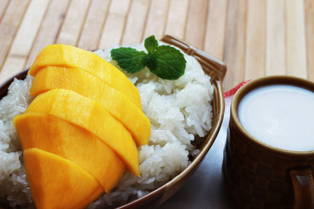 Mango sticky rice is put in a wooden container placed on a brown wooden tableの写真素材