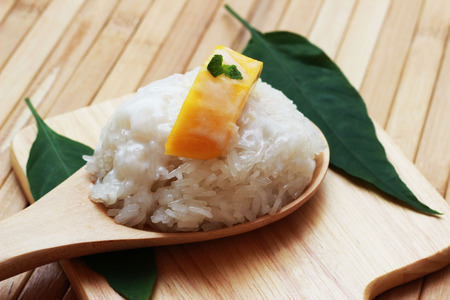 Mango sticky rice is put in a wooden container placed on a brown wooden tableの写真素材