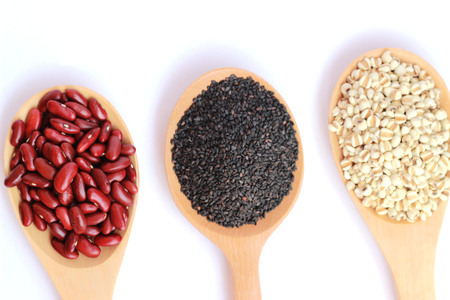 Black sesame, red beans and millet in a brown wooden spoon on a white backgroundの写真素材