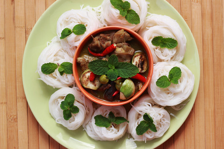 Green curry in an orange cup in the middle of a plate Thai-rice-flour Noodles (kanom jeen)