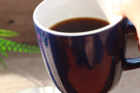 A blue coffee cup with black coffee inside is picked up and placed on a brown tableの写真素材