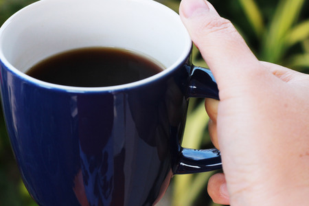 A blue coffee cup with black coffee inside is picked up and placed on a brown tableの写真素材