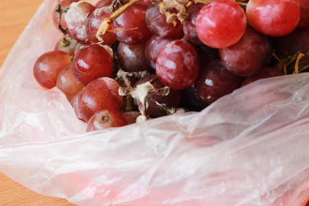 The rotten grapes are molded in a plastic bag on a brown table.の写真素材