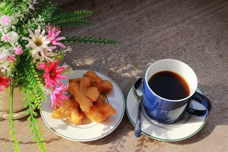 On the brown wooden table there is a blue coffee mug inside, with black coffee and golden fish in the morning.の写真素材