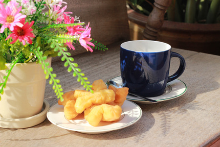 On the brown wooden table there is a blue coffee mug inside, with black coffee and golden fish in the morning.の写真素材