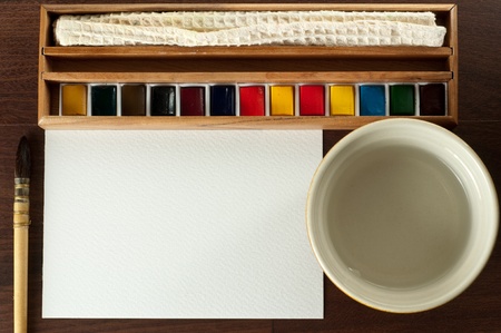 Vintage watercolor paint with cloth, water, brush and blank paper on brown tabel. Top view.の写真素材