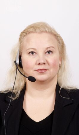 Woman at a helpdesk with headset, dressed in a business suit, serious face while looking at the cameraの写真素材