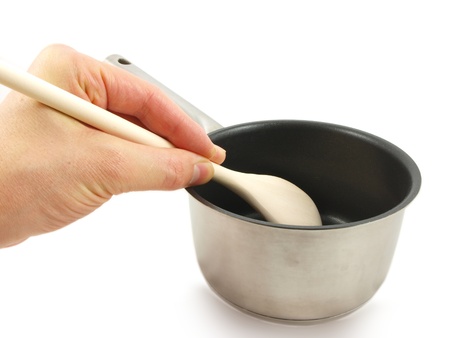 Stainless steel kettle, with wooden spatula and human hand, isolated towards white backgroundの写真素材