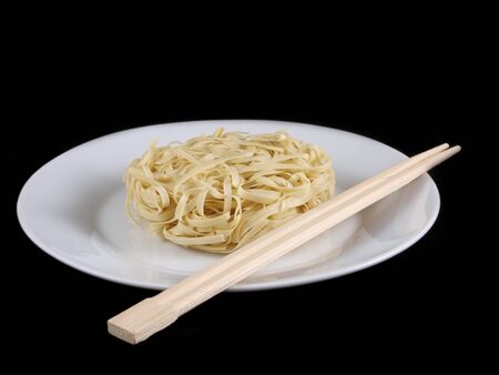 Uncooked noodles, on white plate, with chopsticks, isolated towards black backgroundの写真素材