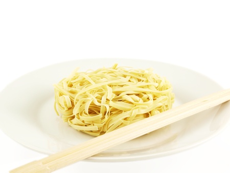 Dried uncoocked noodles, on white plate with chopsticks, isolated towards white backgroundの写真素材