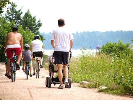 People on bikes, and someone pushing a stroller on a gravel road at summerの写真素材
