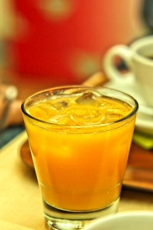 Glass of juice with ice cubes, next to a coffee mugの写真素材