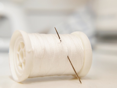 White thread on spool, laying down, with a needleの写真素材