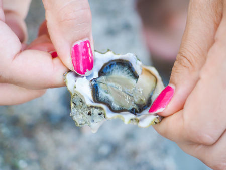 Female person holding an oyster mussel wide open with pink nail paintの写真素材