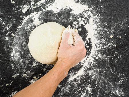 Hands kneading dough on black board with flour