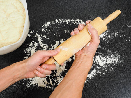 Person preparing a wooden rolling pin with wheat flour before working with the doughの写真素材
