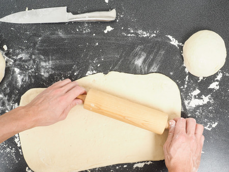 Person handling a dough with a rolling pin floured black tableの写真素材