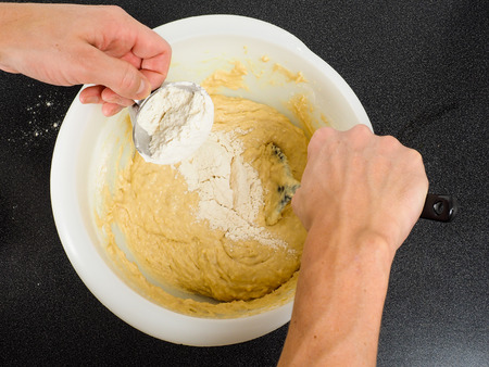 Hands blending flour into a bake mixture with spatula on black tableの写真素材