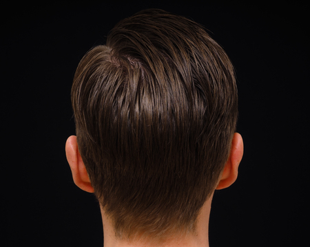 Rear view of hairstyle on male person with brown hair at closeup isolated towards black backgroundの写真素材