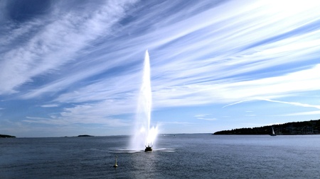 Beautiful fountain spray at sea blending in with stripes of clouds on blue skyの素材