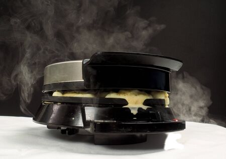 Making fresh steaming hot waffles with a waffle maker towards black on whiteの写真素材