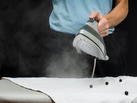 Male person using a steaming hot iron, on a white shirtの写真素材