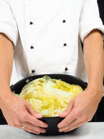 Chef in white jacket holding around a casserole of boiled cabbageの写真素材