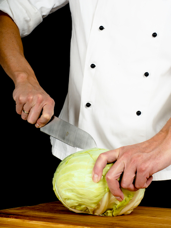 Professional chef holding a sharp cooking knife onto a whole cabbageの写真素材