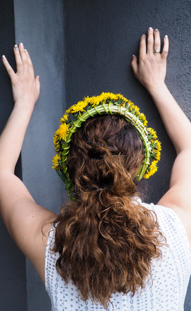 Woman stretching against a grey wall with a flower wreath in beautiful brown curly hairの写真素材