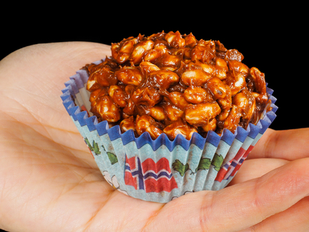 Puffed rice chocolate cake in paper cup with Norwegian flag, in palm, towards blackの写真素材