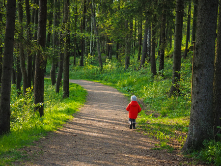 Unrecognizable little boy in a big orange jacket running along on a forestの写真素材