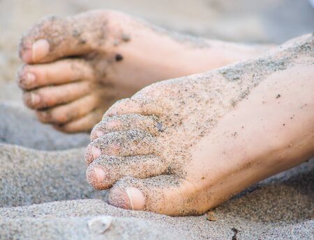 Feet of one unrecognizable caucasian person resting in sand, with wet sand on feetの写真素材