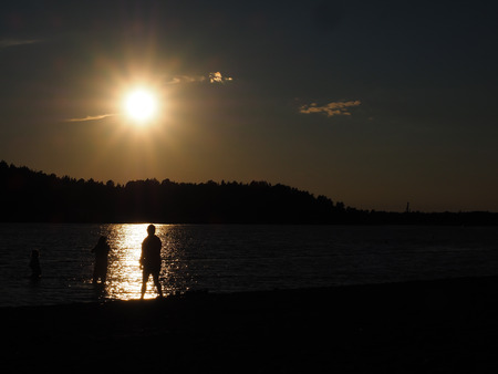 Silhouette of people bathing under late summer sun on a beachの写真素材