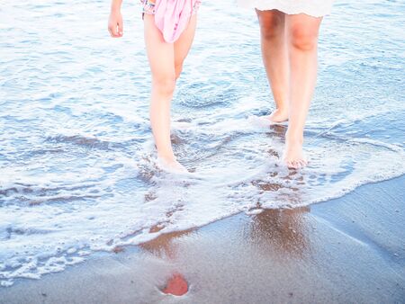 Mother and daughter walking in spuming sea water foam on a beachの写真素材