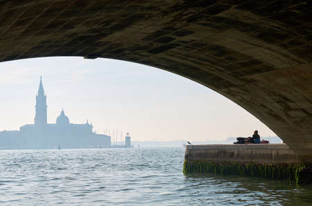 View on a Venice cathedral with two lovers under a bridgeの写真素材